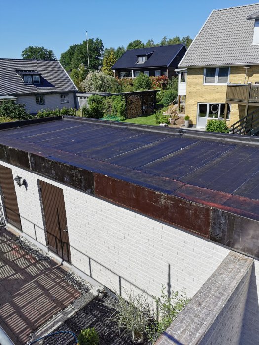 Nytt oavslutat papptak på ett garage med vit tegelvägg, omgivet av grannhus och trädgårdar.