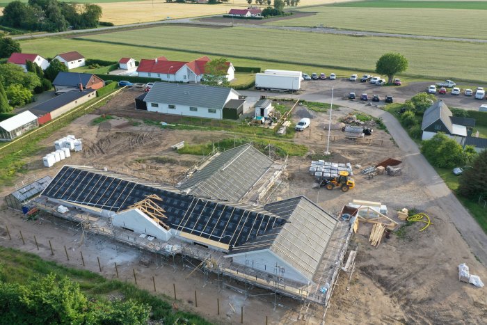 Flygfoto av ett pågående byggprojekt med halvfärdiga byggnader och byggmaterial på en byggarbetsplats.