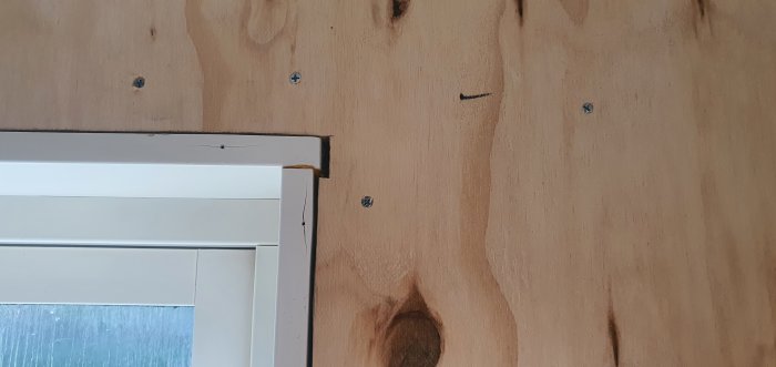 Ett fönster med vita karmar mot en vägg med obehandlat trä, där gips kan monteras kloss an mot karmen.