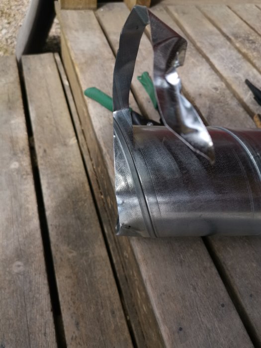 Ventilationsrör med uppmärkta klipplinjer ligger på ett träbord, med sax i bakgrunden.