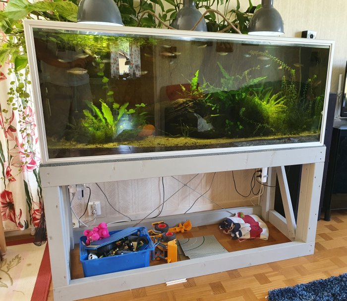 Aquarium på 540 liter och 150x50 cm storlek med växter och reflektorlampor på en vit ställning med verktygslåda under.