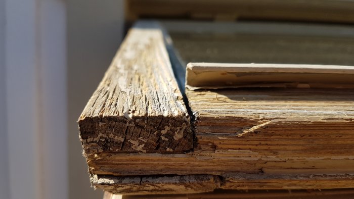 Närbild på ett slitet och torkat träfönster i behov av underhållsmålning, visar sprickor och flagande färg.