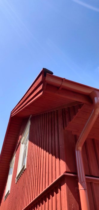 Nybyggt rött hus med vita fönster och tre vindskivor under klarblå himmel.