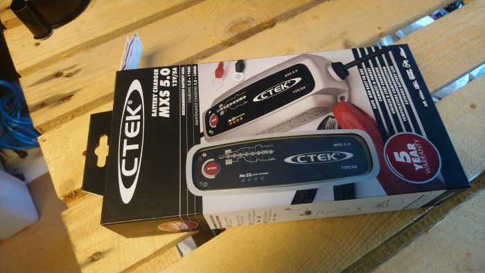 CTEK MXS 5.0 batteriladdare på en träyta, i originalförpackning.