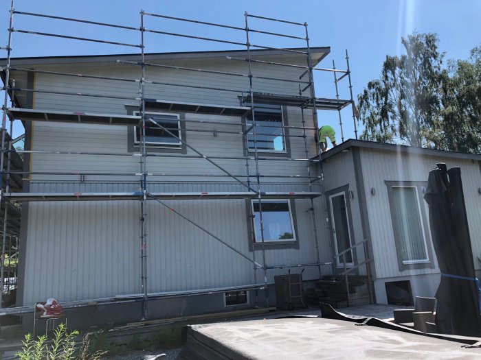 Hus under renovering med tillbyggd övervåning, ställningar, och befintlig fasadbelysning till höger.