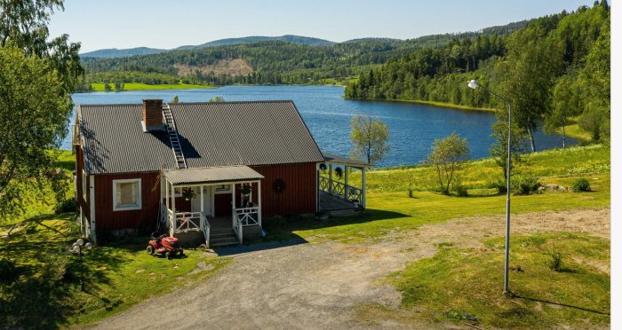 Röd 1 1/2-plans villa med vit veranda och sjöutsikt, stora gräsytor och omgivande natur.