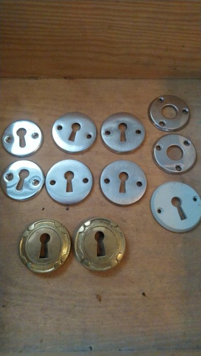 Samling av olika nyckelskyltar i metall på ett träunderlag.