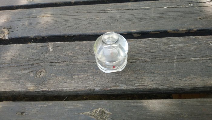 Genomskinlig plastdetalj, troligen inte en gardinstångsknopp, på slitet trä. Pris 5 kr.