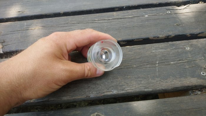 Hand håller en genomskinlig plastdel på ett träbord, misstänkt vara inte en gardinstångsknopp.