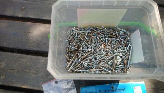 Transparent låda med en blandning av olika typer av skruvar på träbänk, erbjuds för försäljning.