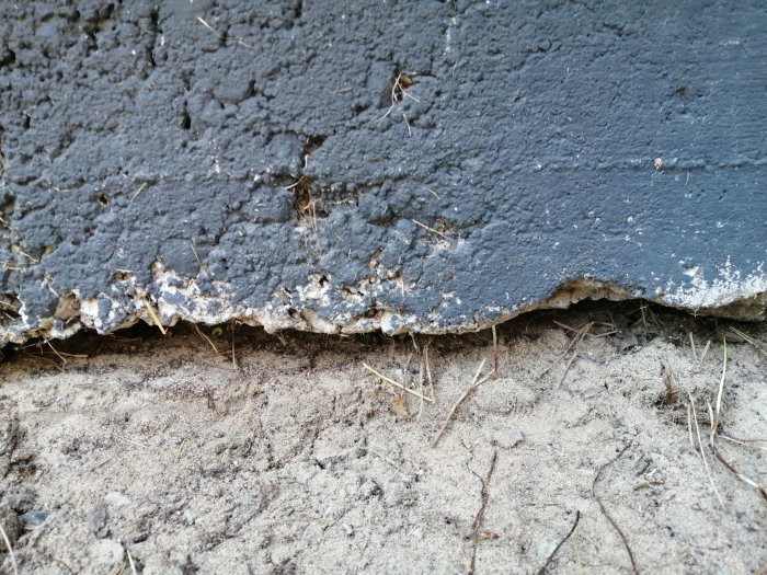 Närbild på skadad betongplatta vid husgrund med synliga sprickor och slitage.
