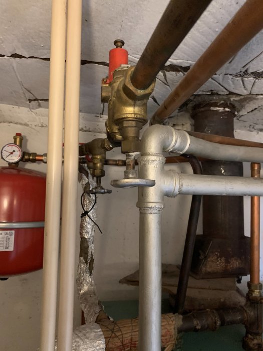 Värmerör och en röd expansionskärl i en källare, vilket antyder frågor om VVS-systemet i ett hus.