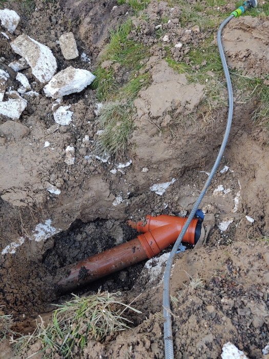 Avgrävd mark med synlig orange avloppsrör Y-koppling som visar tecken på bakfall och dålig installation.