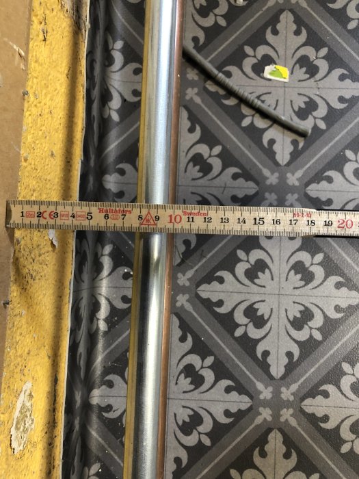 Måttband vid rör på vägg ovanför dekorativt golv, utmaning att bygga ny trappa.