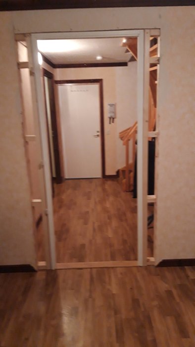Nyinstallerad dörrkarm i en öppning med synlig trappa och dörr i bakgrunden.