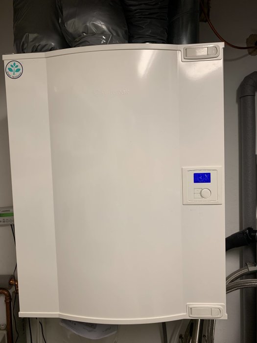 Vit FTX-ventilationsanläggning med kontrollpanel i ett förrådsrum.