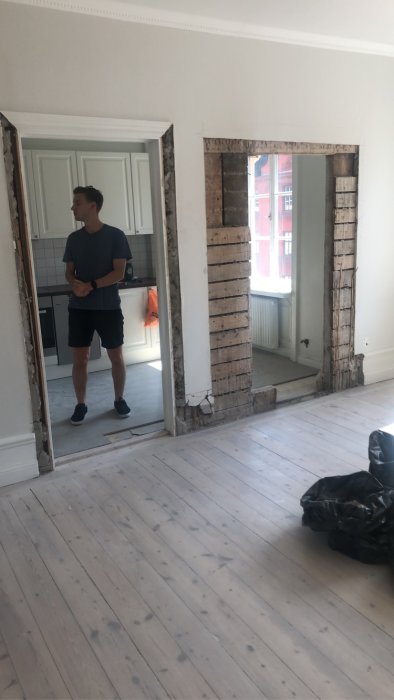 Person i rum med påbörjad väggrivning, synliga vertikala tjocka plankor i två öppningar.