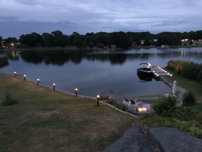 Kvällsbild av en sjö med upplyst stig och båt vid brygga.