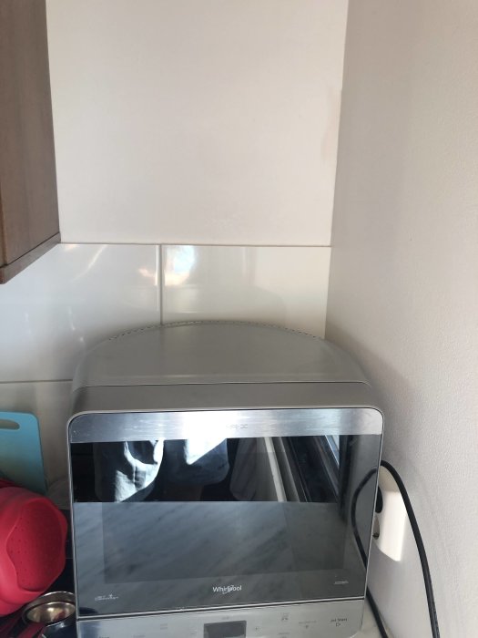 Mikrovågsugn på bänk under köksskåp vid vägg ovanför kakel, plats för hyllplan synlig.