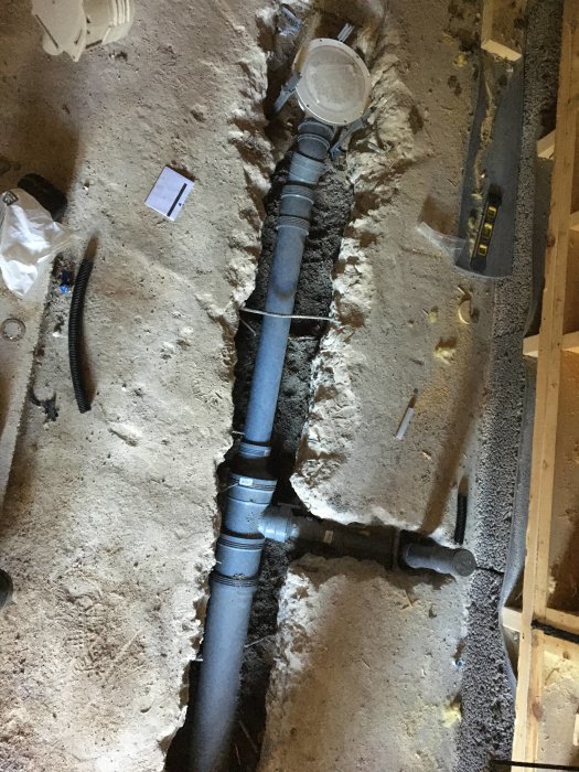 Nytt avloppsrör installerat i grävd ränna med synlig brunn och verktyg.