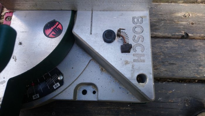 Närbild på en Bosch verktygsdel med nya skadade kol och en skadad kollektor som ligger på träyta.