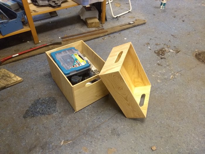 Hemgjorda stapelbara plywoodlådor på ett verkstadsgolv med verktyg inuti en låda.