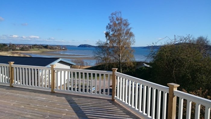 Trästaket med vita vertikala spjälor och naturfärgade stolpar på en terrass med utsikt över havet.