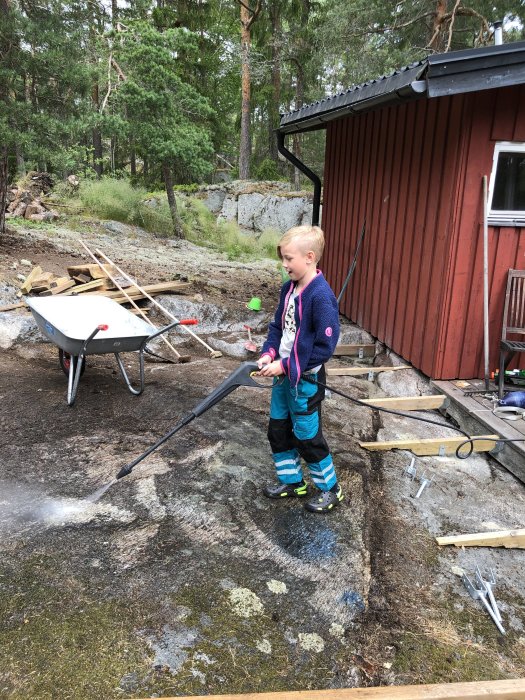 Barn som använder en vattenslang nära ett byggprojekt med trappsteg och verktyg utomhus.