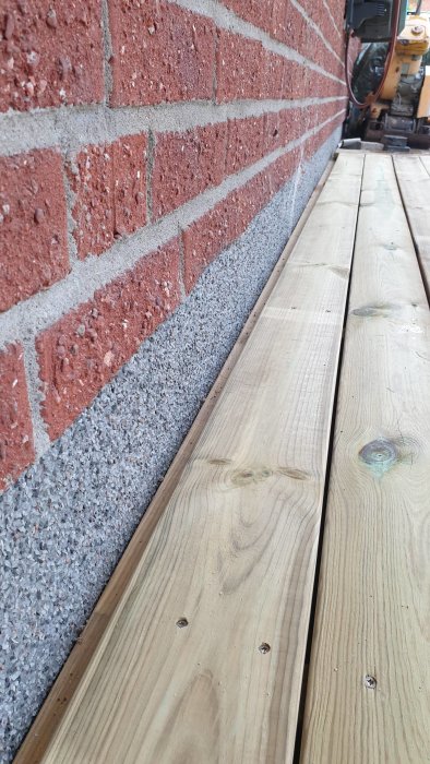 Trallbrädor vid en murad vägg med synlig springa fylld med småsten.