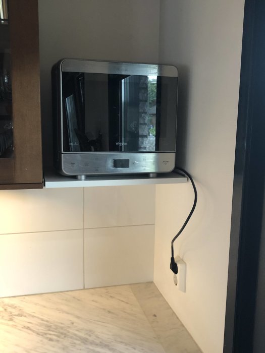 Mikrovågsugn monterad på vägg under skåp med sladd och stickkontakt.