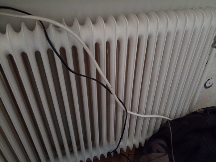 Gammalt vitmålat radiator-/element som täcks delvis av en elkabel och ligger nära fönsterbänk.