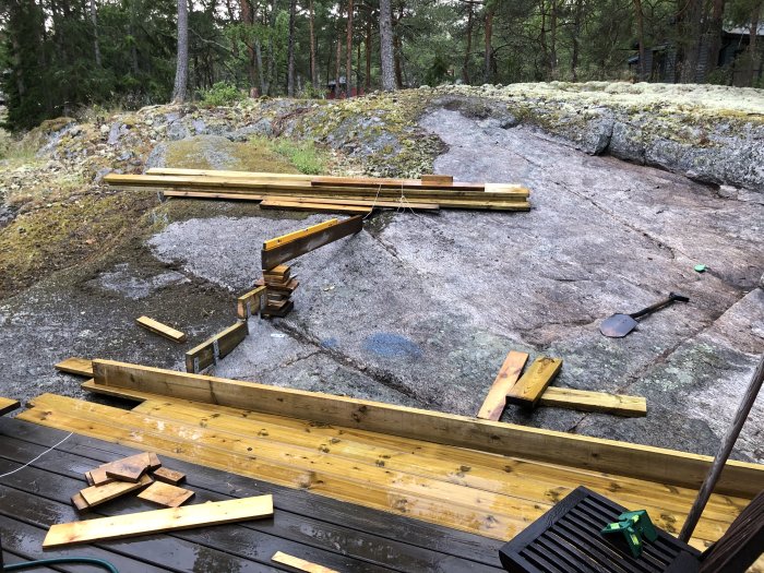 Byggplats med delvis konstruerade trätrappsteg på klippa, verktyg och trämaterial synliga.