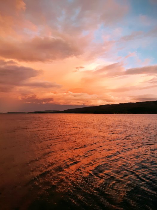 Efterstormens himmel i rosa och orange över ett stilla hav vid solnedgång.