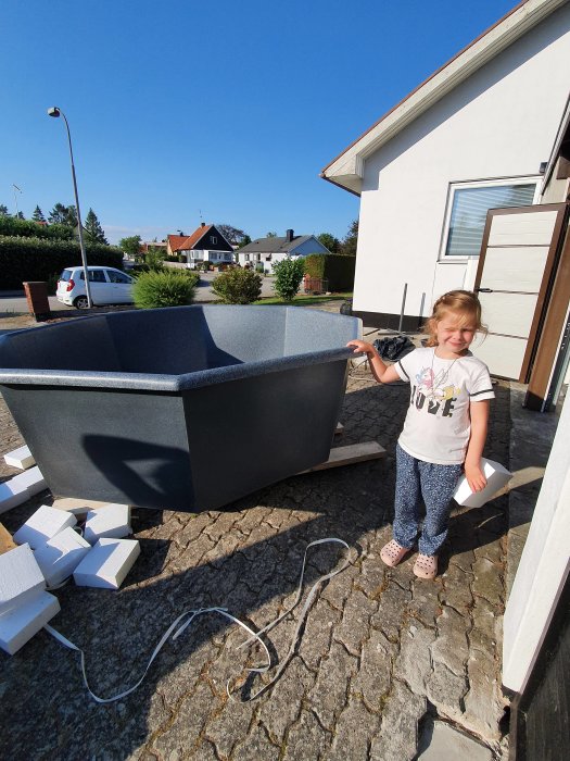 Barn står bredvid en ny polyeten terasspool på en uppfart framför ett hus, i soligt väder.