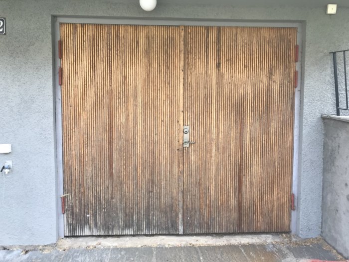 Äldre garageport av teak med vertikala lameller, centralt placerat handtag och lås.