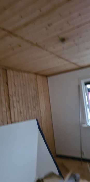 Ett rum under renovering med gammal råspont på väggar och tak samt delvis avlägsnad väggbeklädnad.