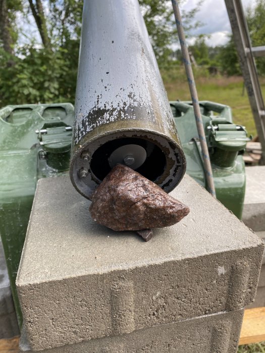 Rostig kil fastklämd i en rörsektion med flagnad färg, uppställd på en betongpelare.