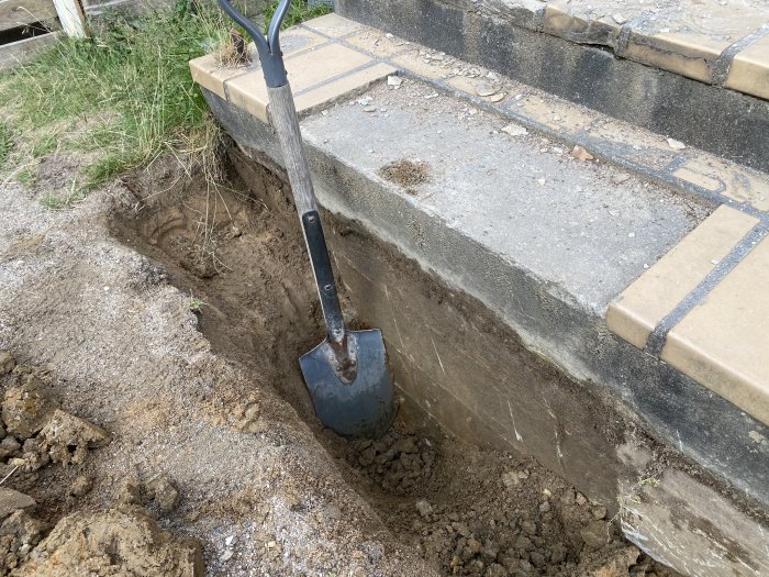 Djup utgrävning vid trappstegs fundament, visar hur tjock och solid konstruktionen är med spade.