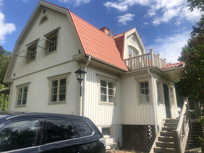 Vit 1940-tals villa med tegelrött tak och beigea fönsterfodringar i solljus.