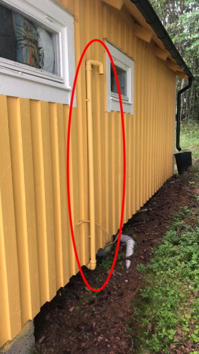 Avloppsrör på utsidan av en gul stuga med potentiell avluftningsproblem markerat med röd cirkel.
