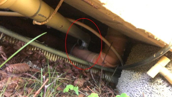 Avloppsrör under hus med misstänkt avluftningsproblem markerat med röd cirkel.