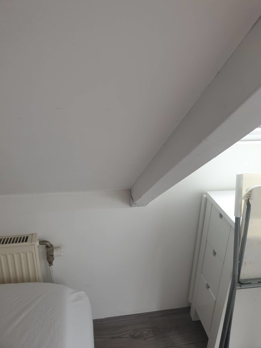 Vinkelrätt vy av ett vindrum med lutande tak och en vit betongvägg som avslutar rummet diagonalt mot bjälken.