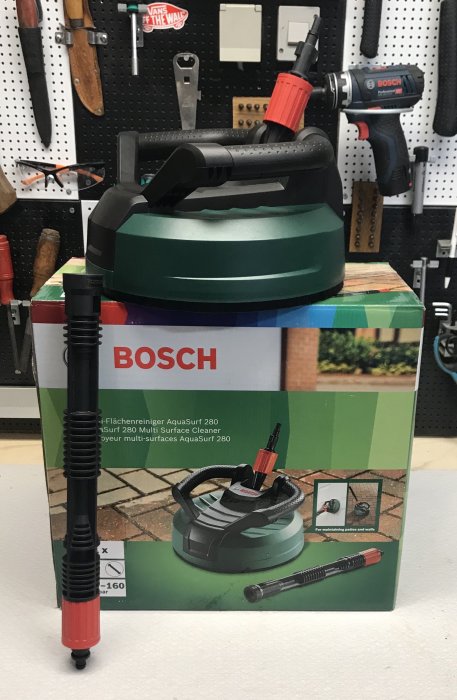 En Bosch terasstvätt AquaSurf 280 förpackning framför verktygstavla.