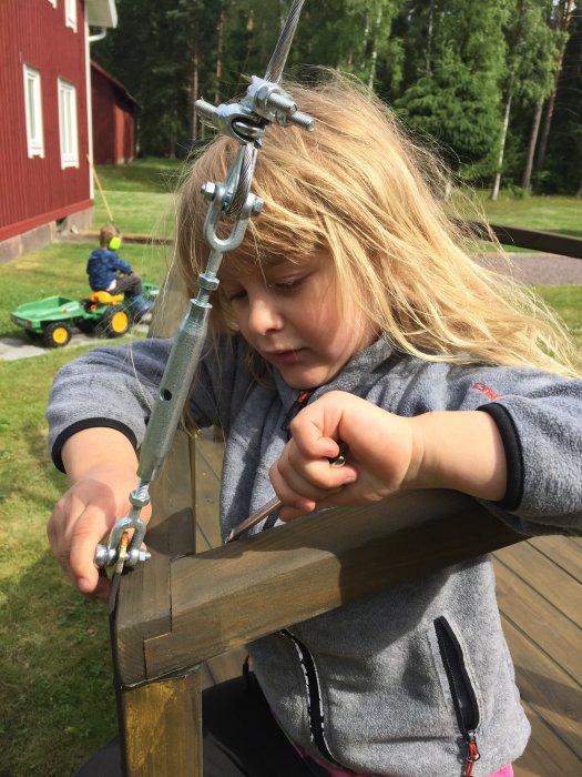 Barn justerar vantskruv på en trälåda som representerar en masttopp ute i trädgården.