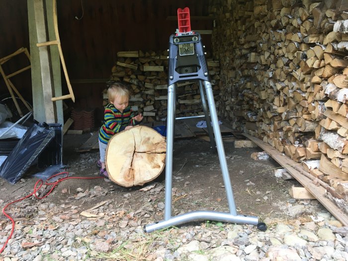 Barn står bredvid AL-KO 520/5 vedklyv framför vedstapel med en stor vedklabb redo för klyvning.