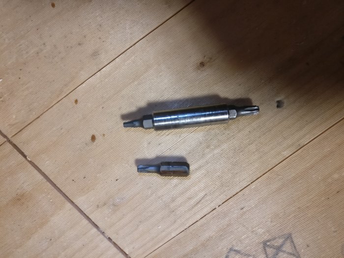 Dubbel bitshållare och skruvbits insatta i träyta, betoning på bitshållarens runda form.