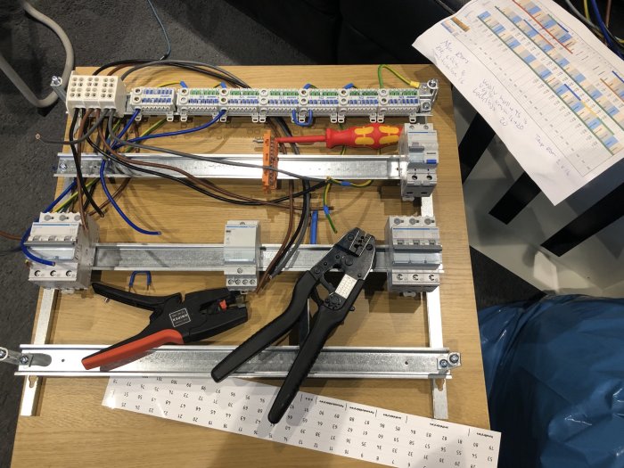 Elinstallation med kablar, kopplingsdosa och verktyg på arbetsbord med schema.