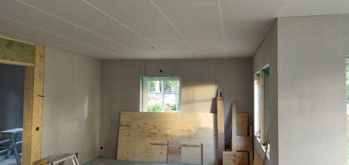 Ett rum under renovering med nymonterade gipsskivor på taket och oskyddade väggar.