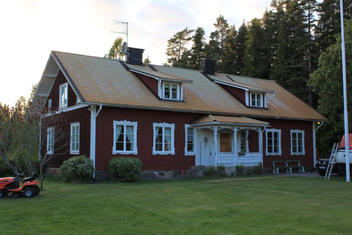 Röd trävilla med ett slitet aluminiumtak som uppvisar färgsläpp och mattning under en skymningshimmel.