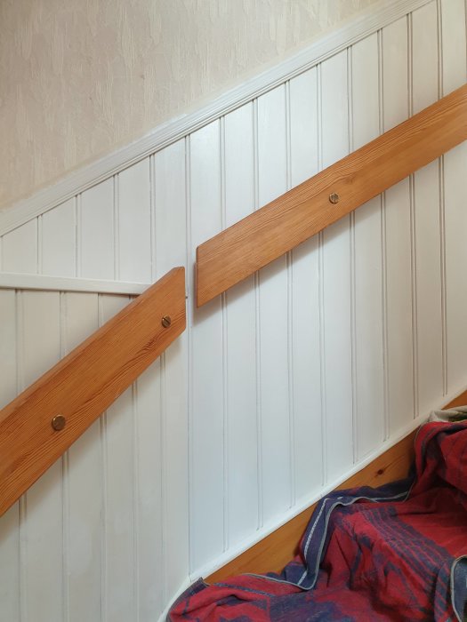 Vägg delvis täckt med träpanel som har målats vit, skyddslakan nedtill. Trälist i mitten som ej målats.